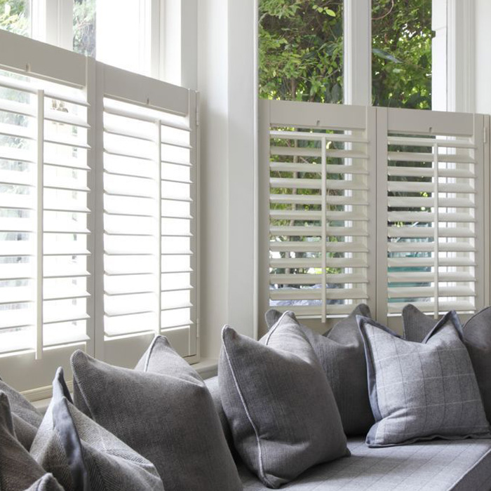 White polywood shutters by a long window seat with blue and white throw pillows.