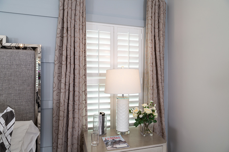 white plantation shutters with curtains over small window in a bedroom