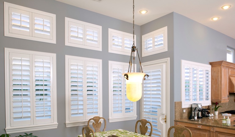 Shutters can fix both sun glare and heat loss problems. White plantation shutters in dining room