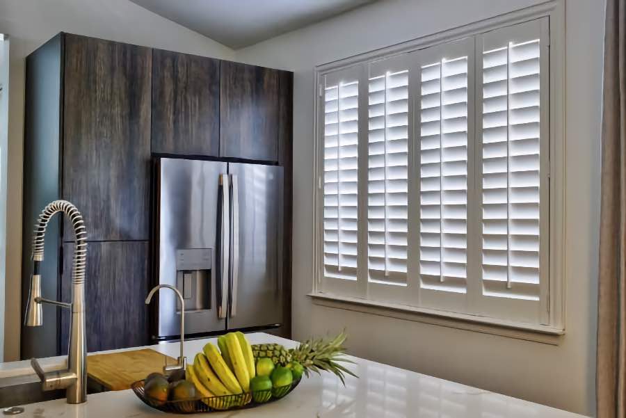 Homeowners use indoor window shutters in Chicago when they want attractive and functional window treatments. Polywood shutters on a large kitchen window
