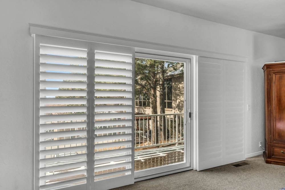 White plantation shutters covering a sliding door in a living room area